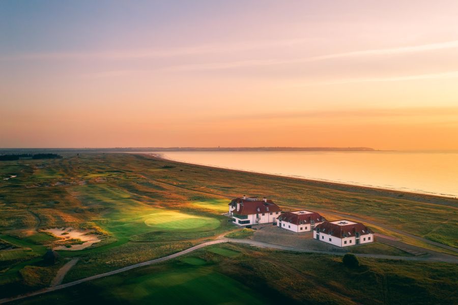 An aerial shot of three white buildings set within a golf course and the sea beyond.