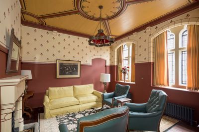 A sitting room with Victorian decor, a yellow sofa and blue chairs