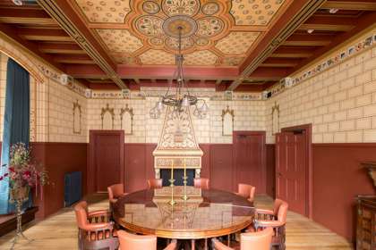 A room with a decorated painted ceiling, ornate walls and circular dining table and chairs.