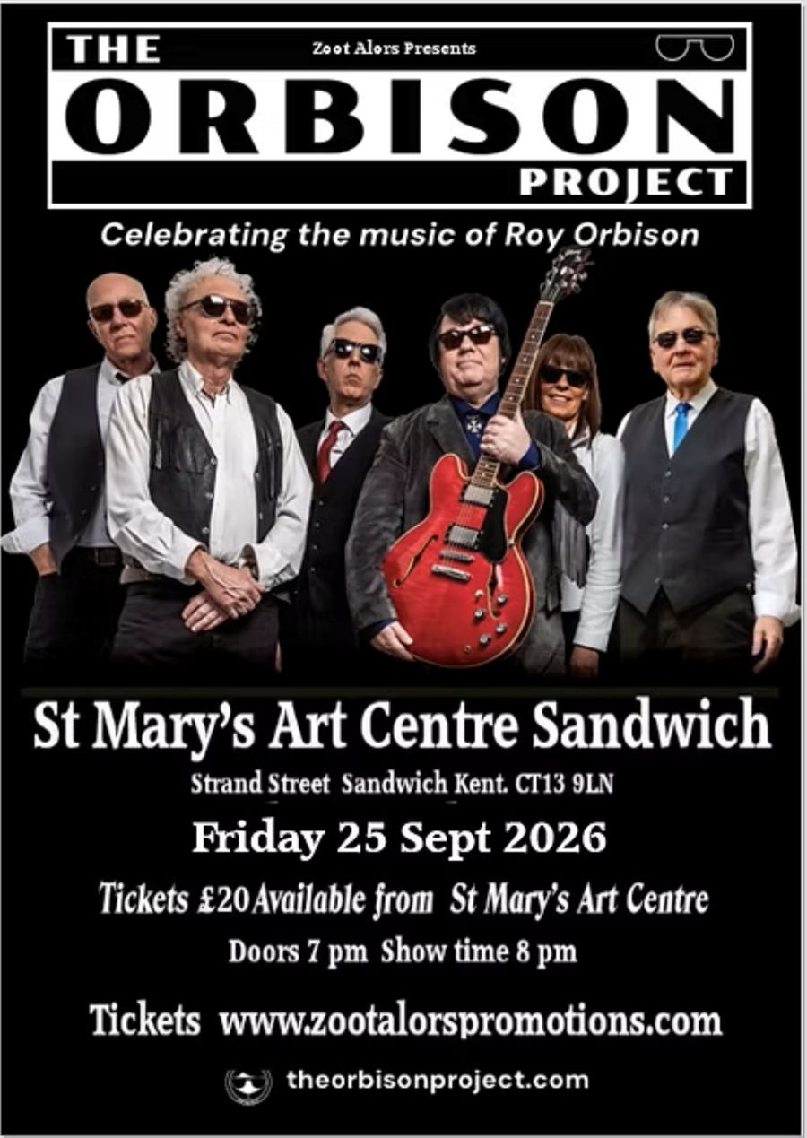 6 musicians stood in a group with a Roy Orbison look alike holding a red guitar