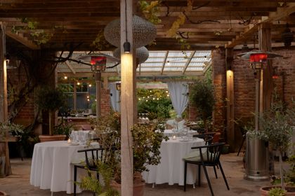 Restaurant tables in a courtyard setting under a wooden pergola with climbing plants.