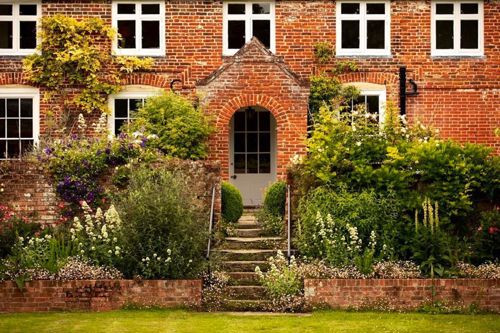 Front of Updown Farmhouse with mature garden, flower boarders and steps leading up to the front door.