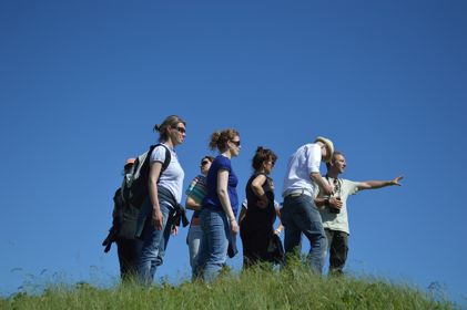 A group of people outdoors all looking in the direction the group leader is pointing. 