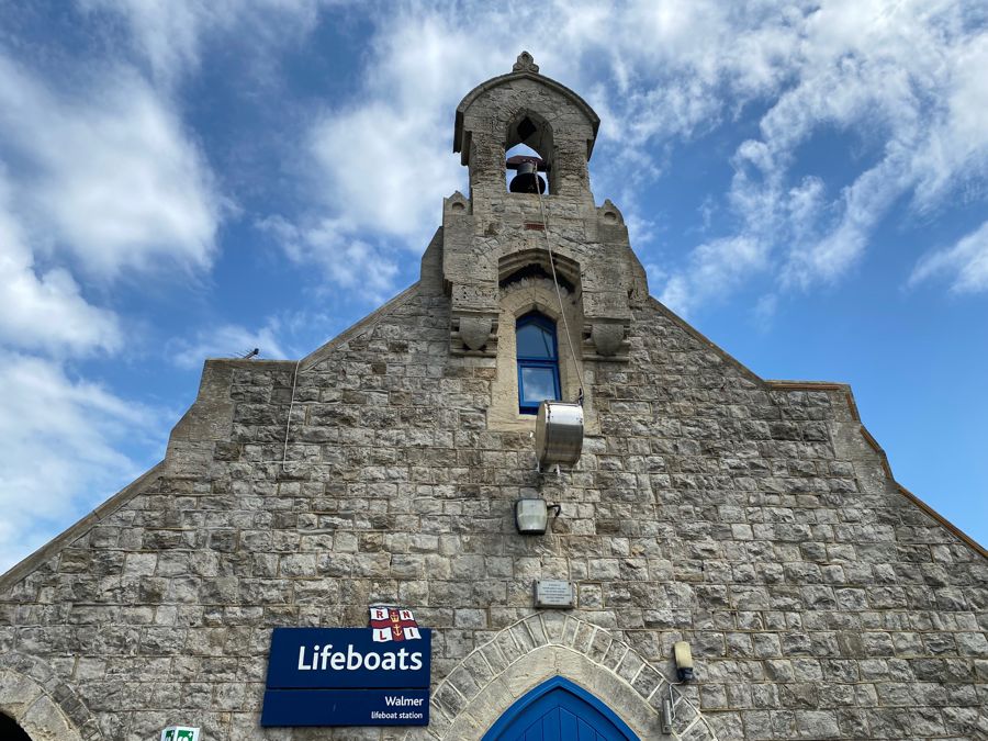 A grey stone building with a bell at the top and a sign saying Lifeboats.
