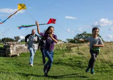 Two children and an adult running along with kites