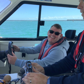 A smiling man in a wheelchair piloting a boat.