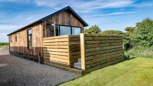 A wooden lodge set on a gravel drive next to a green field