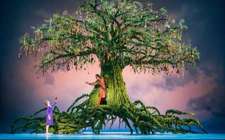 A scene from the ballet with a large green tree on stage with 2 ballet dancers