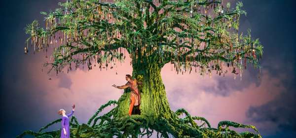 A scene from the ballet with a large green tree on stage with 2 ballet dancers