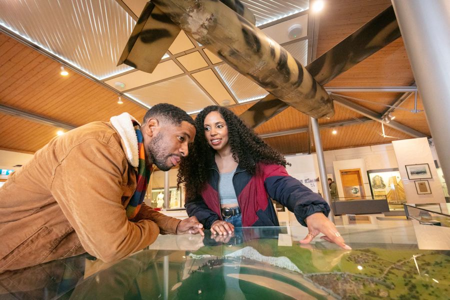 A couple leaning over a model map of the coast in the history gallery at Dover Museum with a replica doodlebug overhead